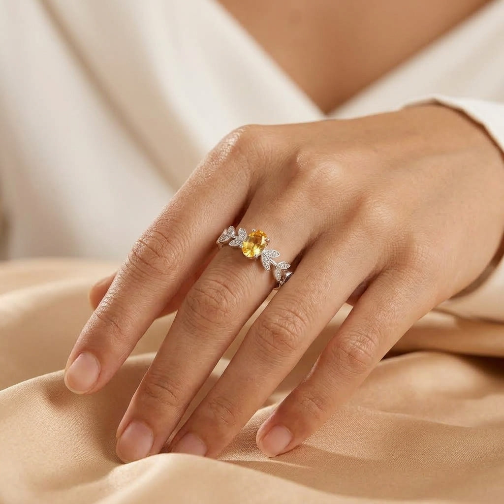 Bague Abondance Dorée en argent ornée d'une pierre citrine ovale centrale et de détails en forme de feuilles serties de zircons scintillants portée sur un doigt