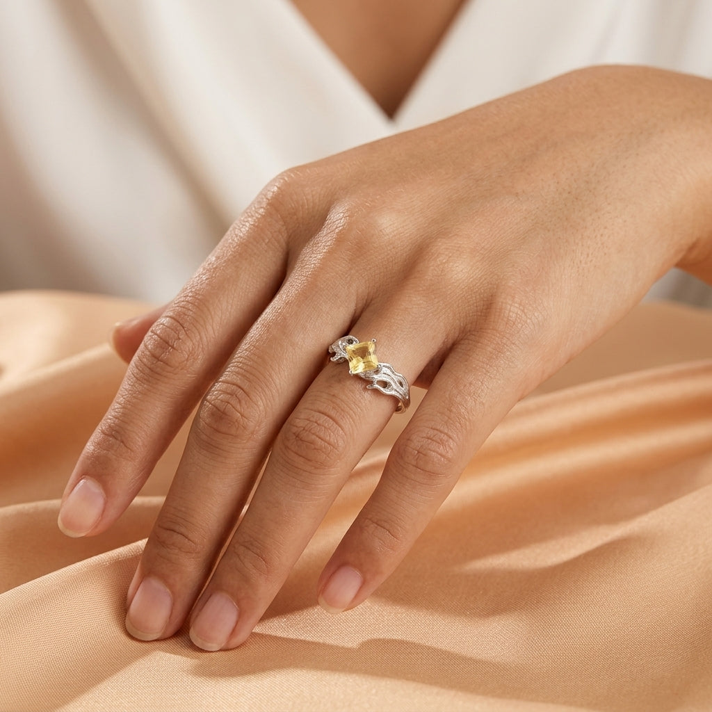 Bague Éclat de Joie en argent avec une pierre citrine jaune carrée portée au doigt sur fond en tissu satiné.