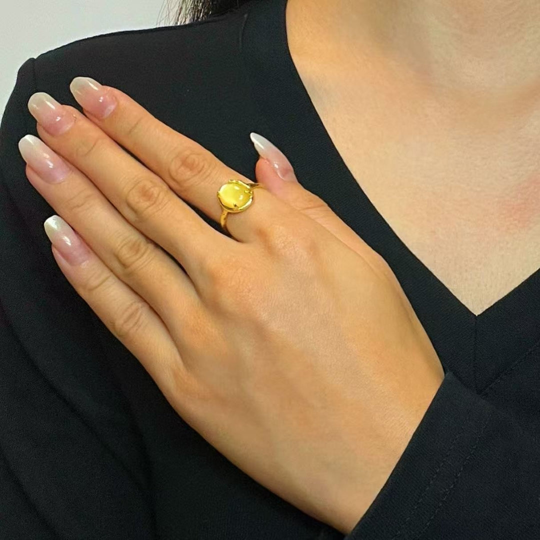 Gros plan d'une main portant une bague plaquée or avec une pierre citrine jaune ovale et une incrustation de nacre.