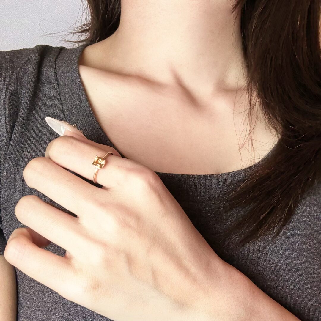Bague fine plaquée or avec une citrine carrée lumineuse portée à l'annulaire d'une main posée sur la poitrine.