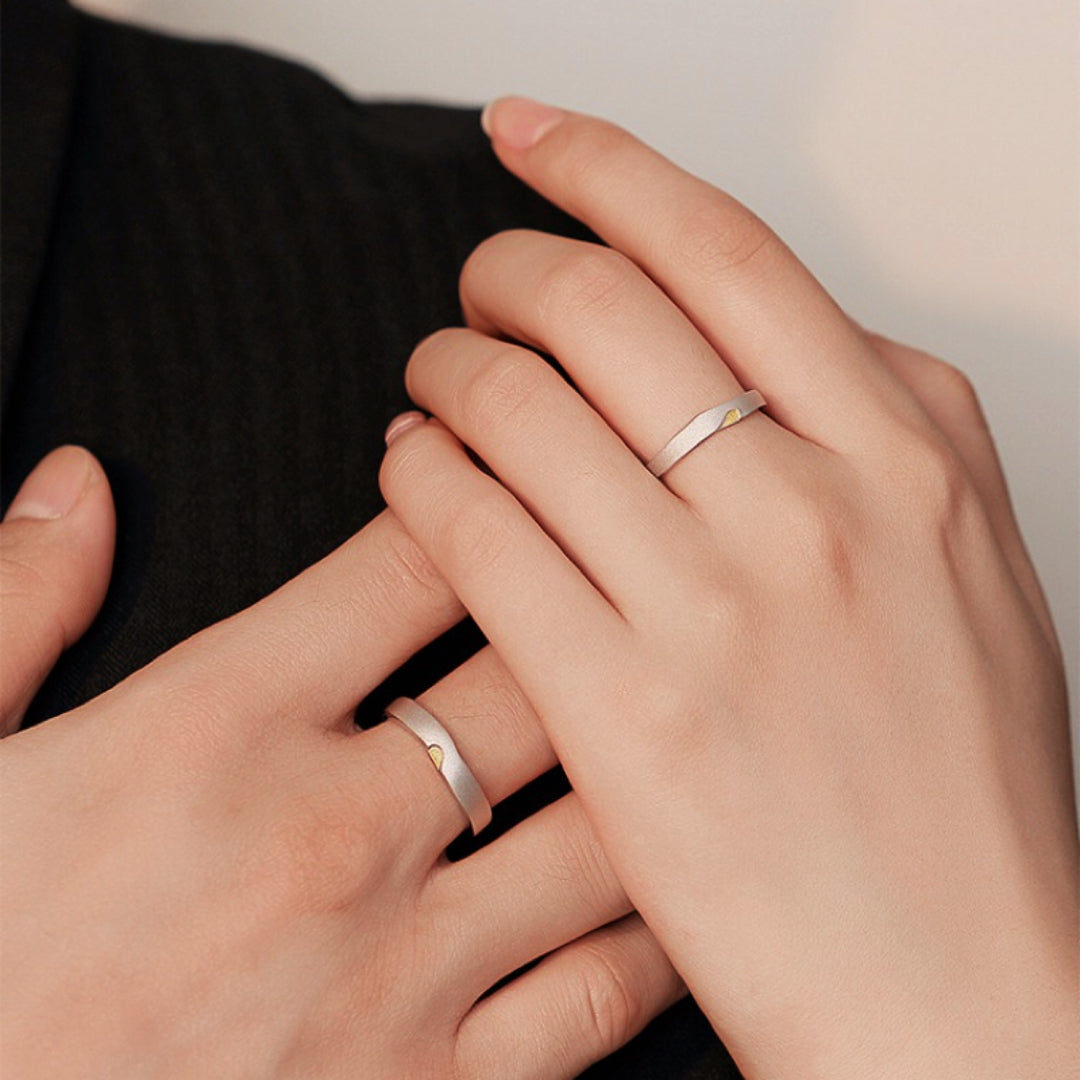 Deux bagues de couple en argent ornées d'un petit soleil jaune, portées par un homme et une femme.