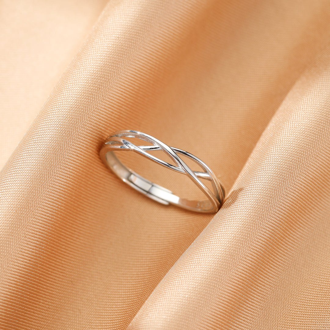 Bague d'argent pour couple au design entrelacé, posée sur un fond de tissu satiné couleur pêche.