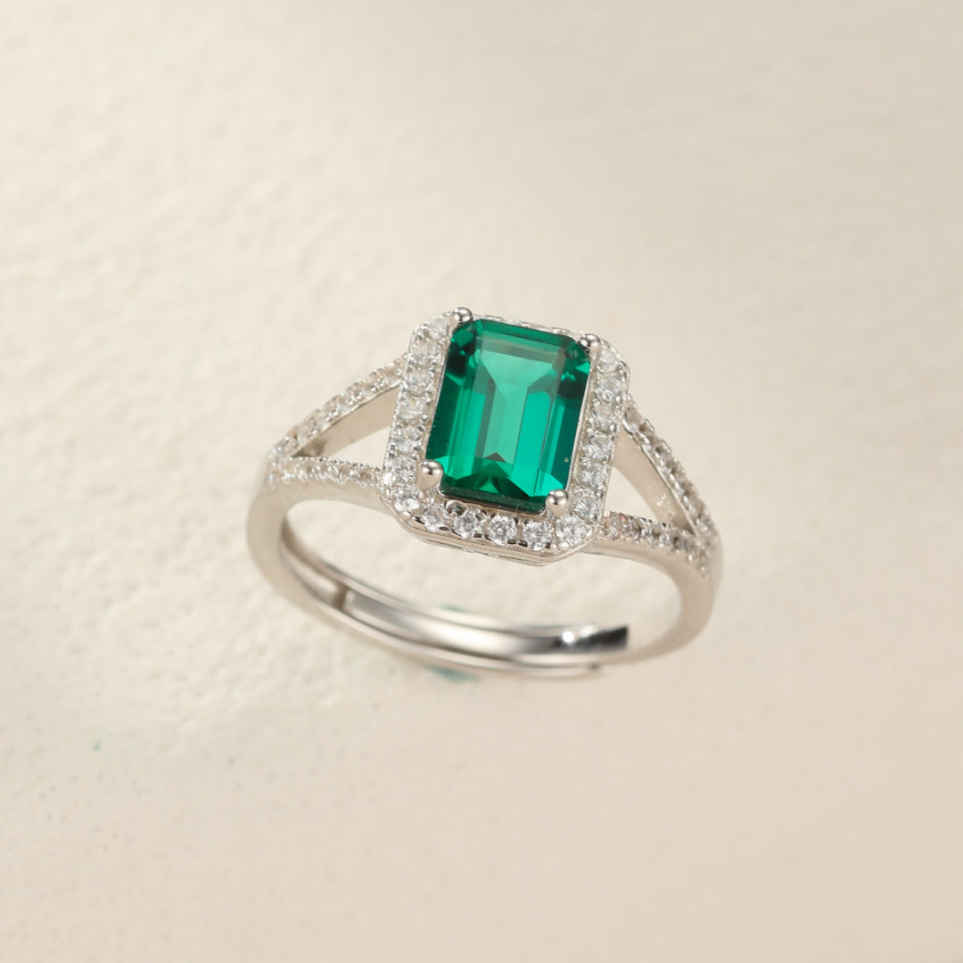 Bague en argent 925 sertie d'une émeraude rectangulaire centrale entourée de petits cristaux scintillants.