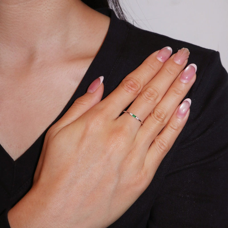 Bague fine en argent 925 sertie d'une émeraude rectangulaire et de petits diamants, portée à l'annulaire d'une main manucurée.
