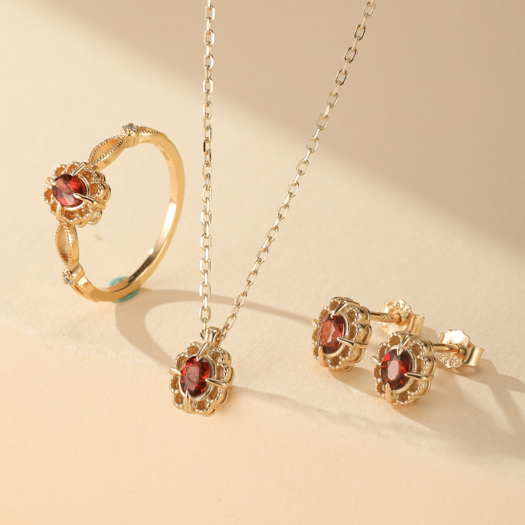 Ensemble de bijoux en plaqué or avec une bague, un collier et des boucles d'oreilles sertis d'une pierre de grenat rouge et de petits diamants.