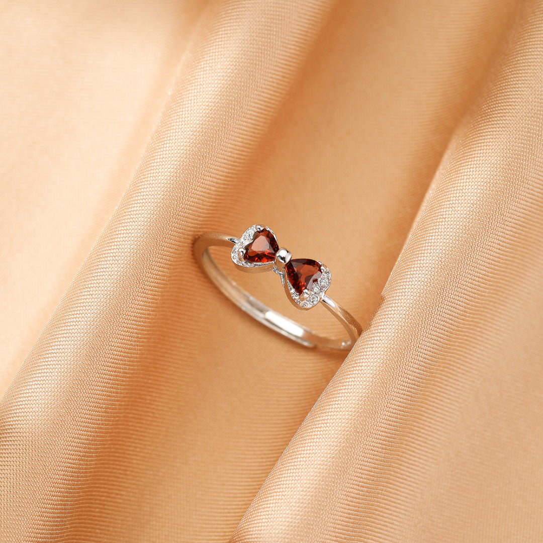 Bague en argent ornée de deux grenats en forme de cœur formant un nœud, sertie de petites pierres scintillantes.