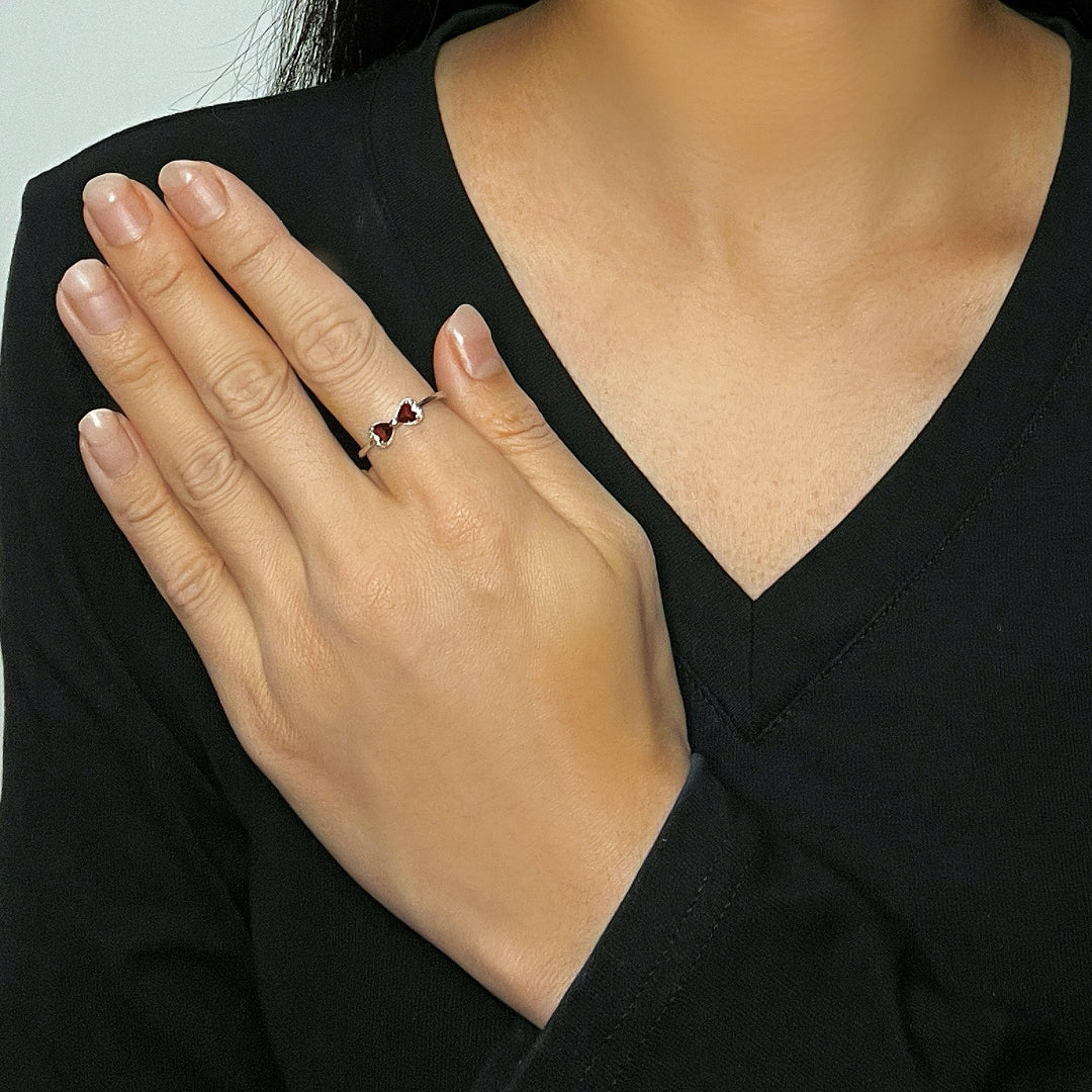 Bague en argent ornée de deux grenats en forme de cœur, évoquant un nœud, portée au doigt d'une femme.