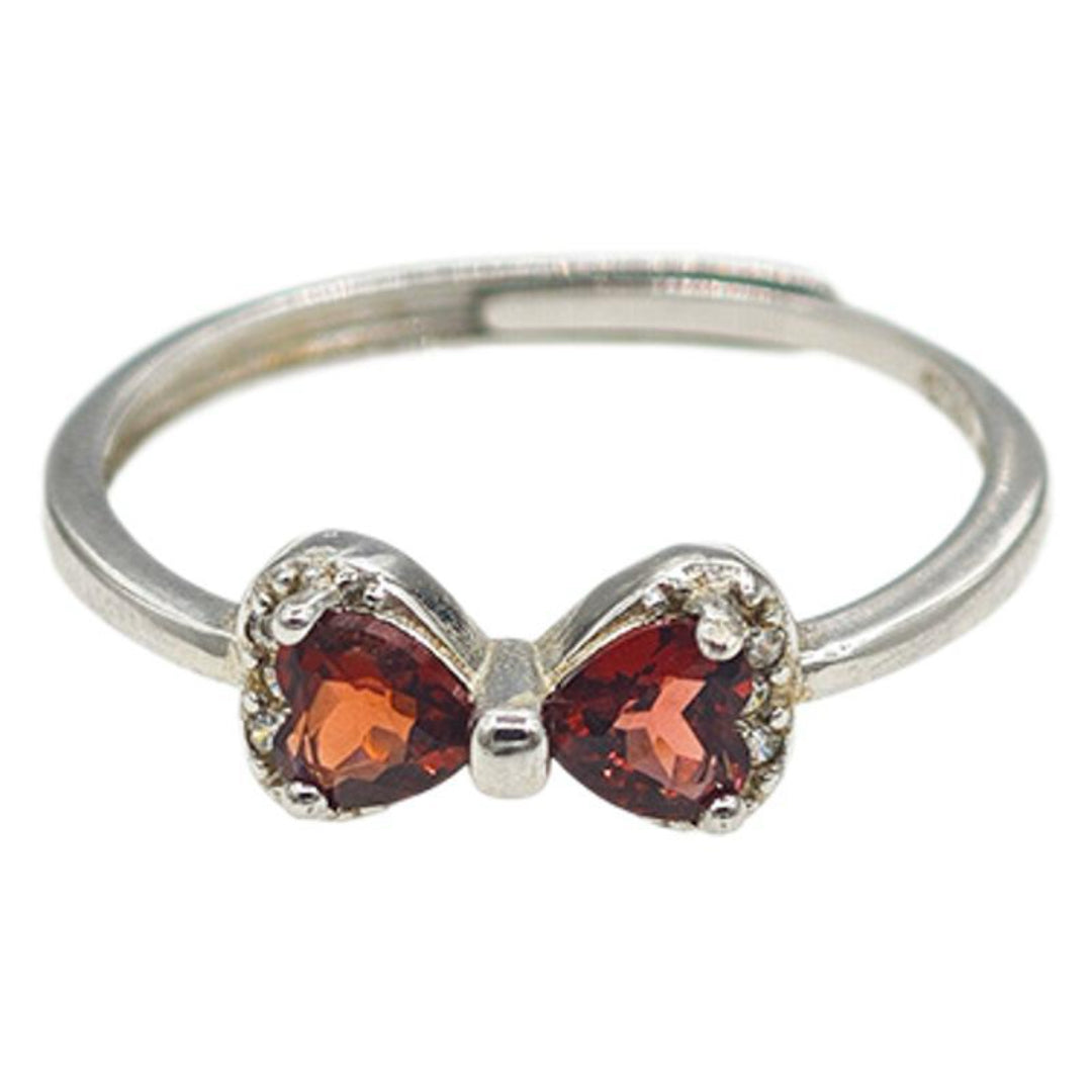 Bague en argent ornée d'un nœud en forme de cœur avec deux grenats rouges sertis et de petites pierres blanches scintillantes sur les côtés, sur fond blanc.