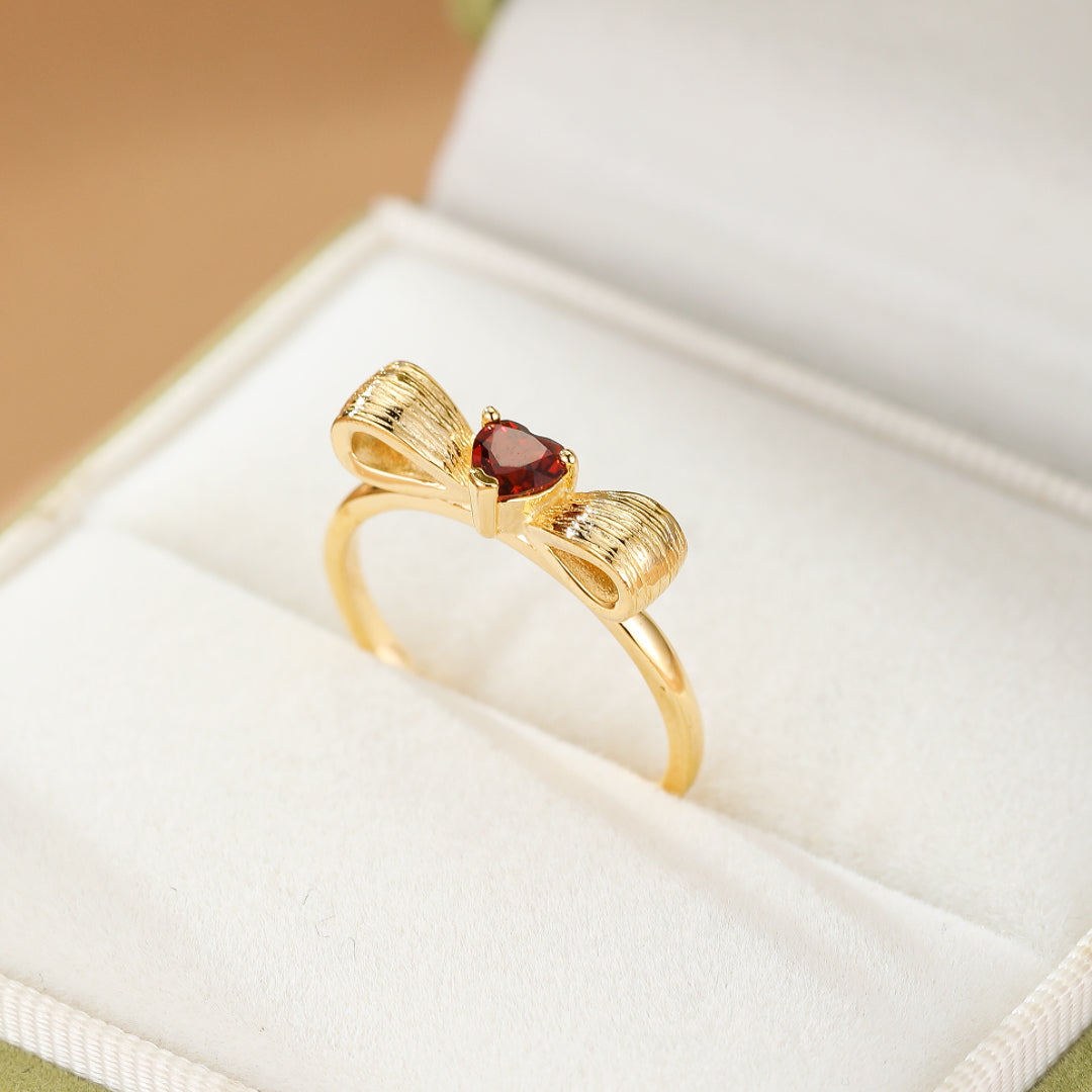 Bague en argent plaqué or ornée d'un nœud texturé serti d'une pierre grenat en forme de cœur.