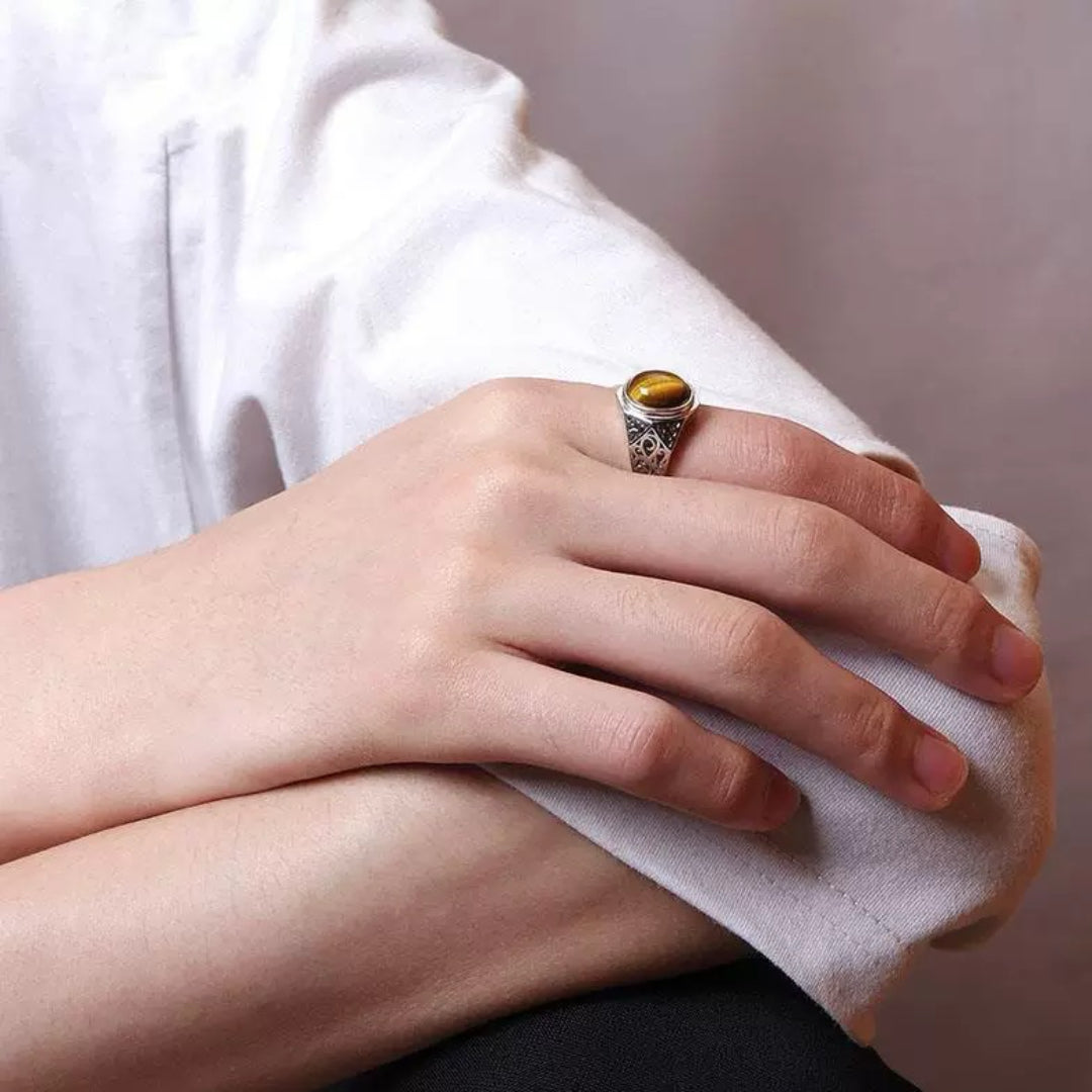 Bague pour homme en argent ornée d'une pierre d'œil de tigre ovale et d'un motif gravé sur les côtés, portée à l'annulaire.