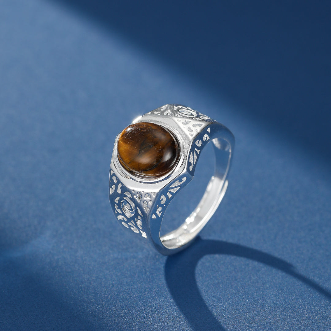 Bague homme en argent ornée d'une pierre d'œil de tigre naturelle avec des motifs gravés sur le côté, sur fond bleu