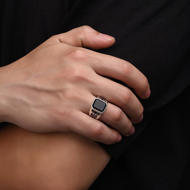 Bague pour homme avec pierre onyx noire rectangulaire et motifs gravés sur l'anneau en argent porté sur le doigt
