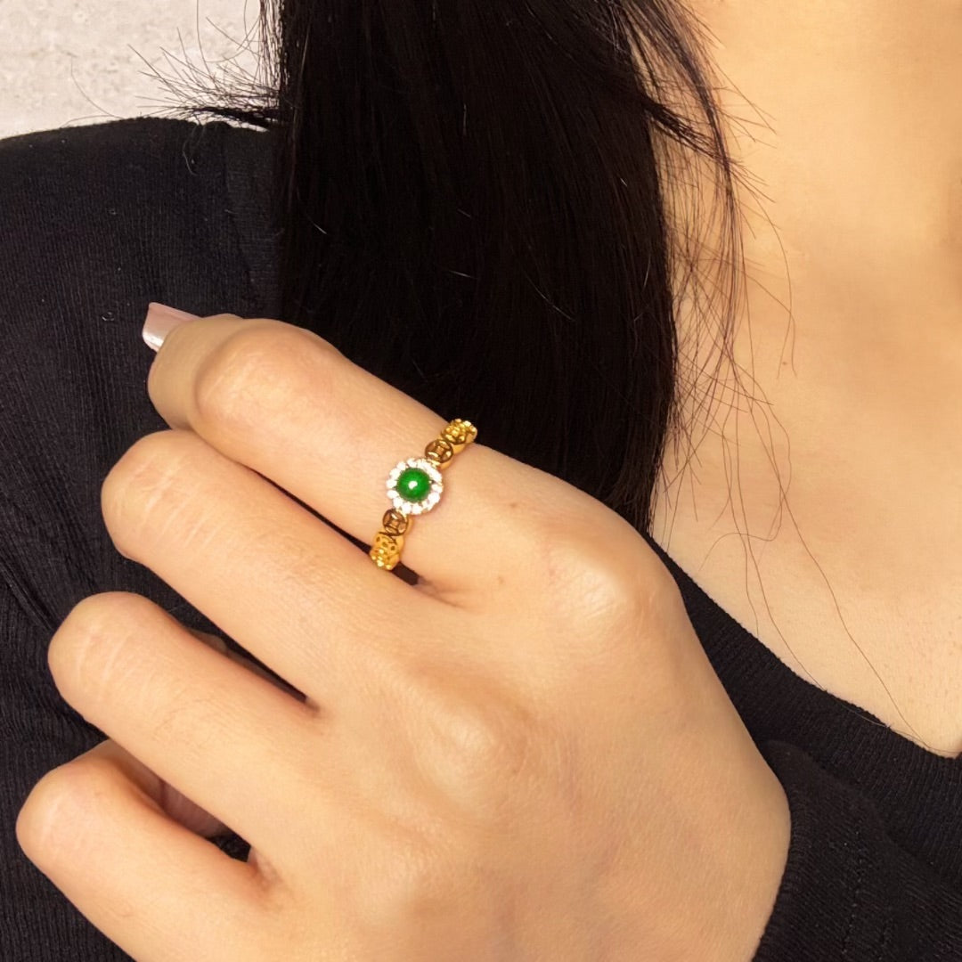Bague en argent plaqué or sertie d'un jade rond vert entouré de petits diamants, portée au doigt d'une femme.