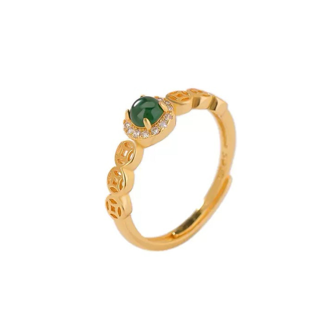 Bague ajustable plaqué or sertie d'une pierre de jade verte ronde entourée de petits cristaux et ornée de motifs de pièces chinoises sur l'anneau.