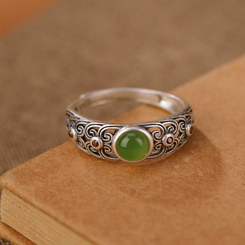 Bague en argent plaqué or avec un jade rond central et des détails gravés ornés de petites pierres rouges.
