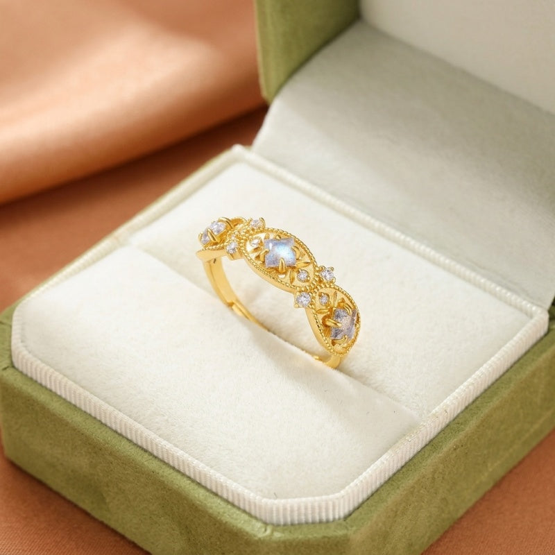 Bague en argent plaqué or avec une labradorite centrale et de petites pierres d'accent, dans un écrin vert.