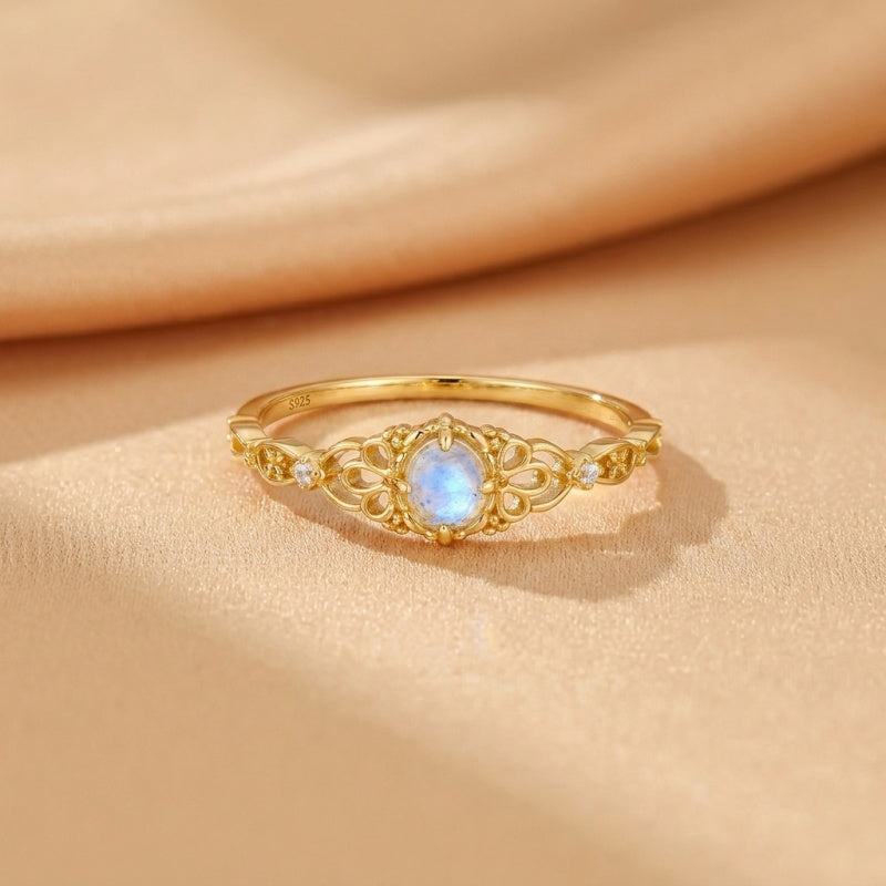 Bague en argent sterling 925 plaqué or avec une pierre de lune bleue ovale et des détails filigranes, rehaussée de petites pierres d'accent.