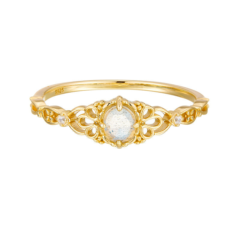 Bague fine en or avec une pierre de labradorite ovale au centre, entourée de motifs floraux ajourés et de deux petits zircons cubiques de chaque côté.