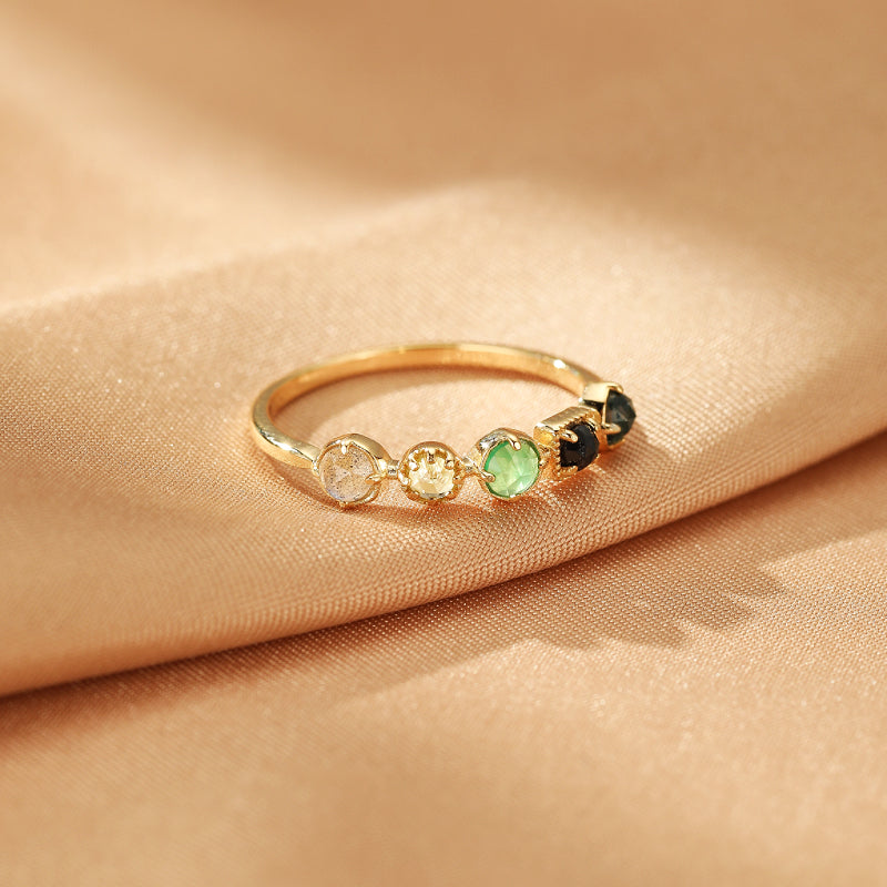 Bague en or fin sertie de cinq pierres rondes : labradorite, chrysoprase et péridot, sur un fond satiné.