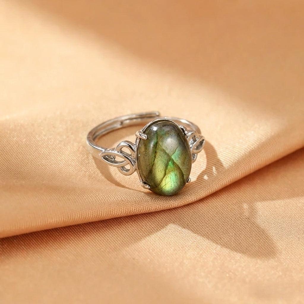 Bague en argent ajustable avec une labradorite ovale aux reflets verts et bleus, posée sur un tissu satiné couleur miel.