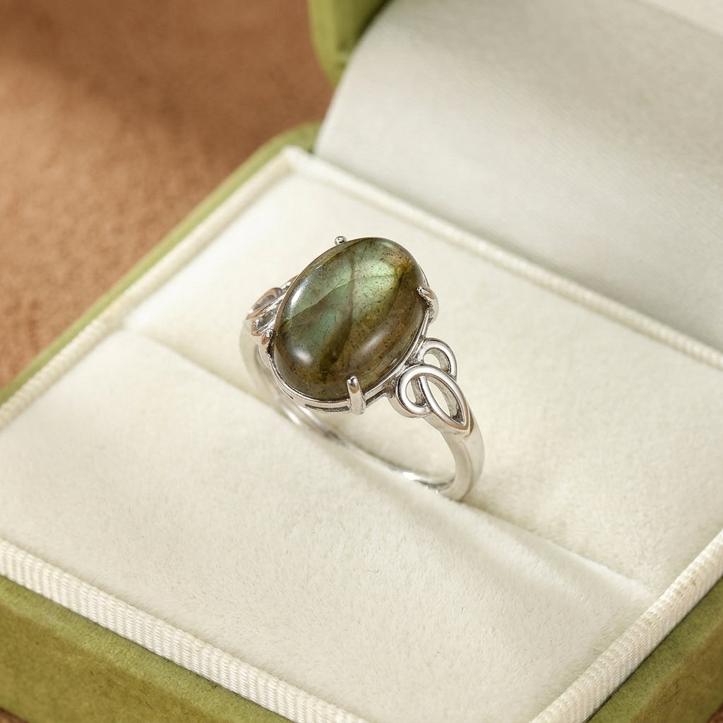 Bague en argent avec une grande labradorite ovale aux reflets verts et bleus, posée dans un écrin vert.