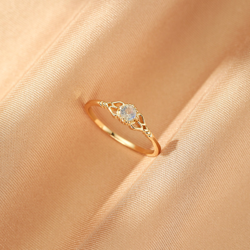 Bague fine en argent plaqué or sertie d'une pierre de lune ronde et chatoyante, avec un design ajouré délicat sur les épaules de la bague.
