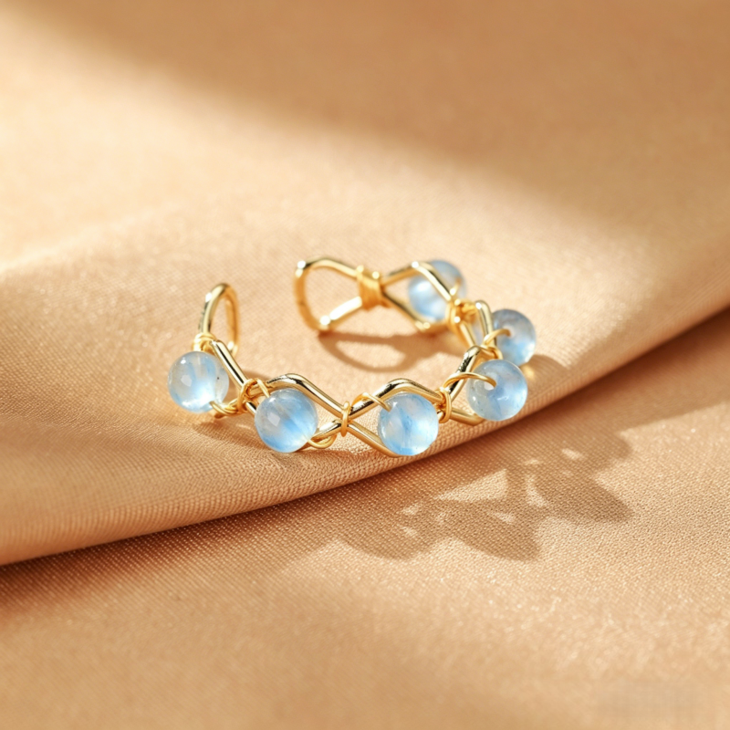 Bague ouverte en plaqué or avec des perles rondes de labradorite bleue disposées en forme de cercle, sur un fond de tissu satiné beige.