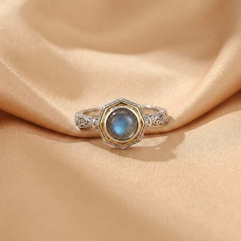 Bague en argent plaqué or sertie d'une pierre de labradorite bleue aux reflets profonds, avec une monture octogonale ornée de motifs gravés.