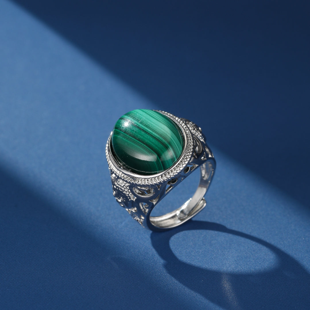 Bague en argent 925 ornée d'une pierre de malachite verte aux motifs naturels, sur fond bleu avec un jeu d'ombres.