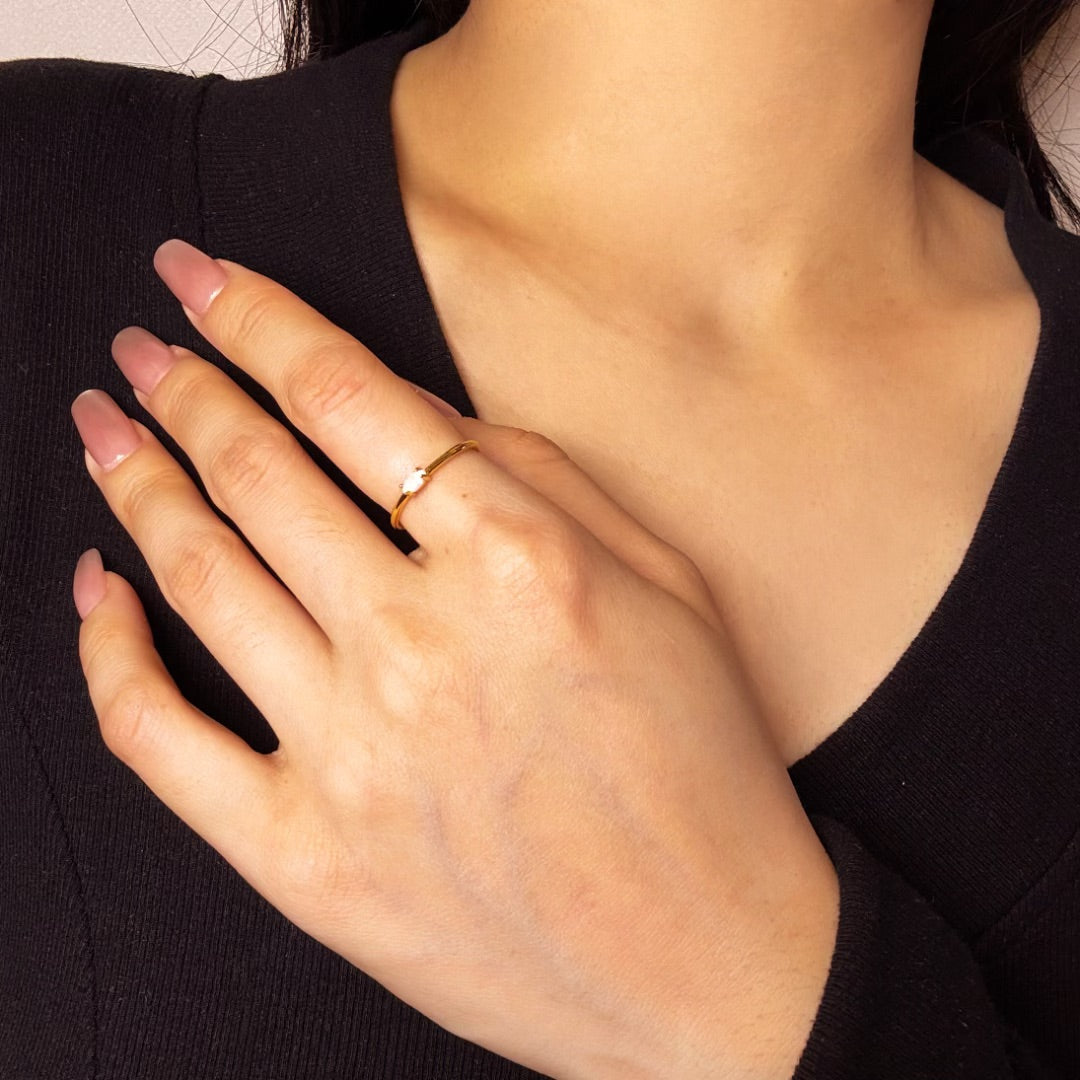 Bague fine en argent plaqué or avec une opale solitaire portée au doigt.