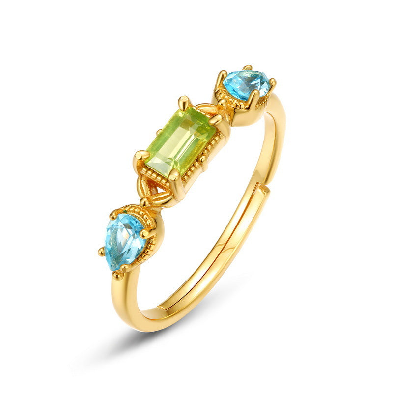 Bague en argent plaqué or sertie d'une pierre centrale rectangulaire vert péridot et de deux pierres latérales bleues en forme de goutte de topaze, avec des détails géométriques.