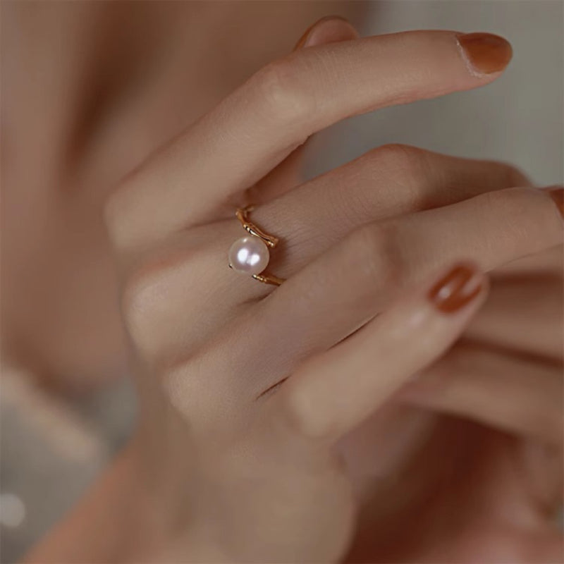 Bague élégante en argent plaqué or avec une perle blanche discrète, design inspiré du bambou, portée sur une main aux ongles vernis marron.