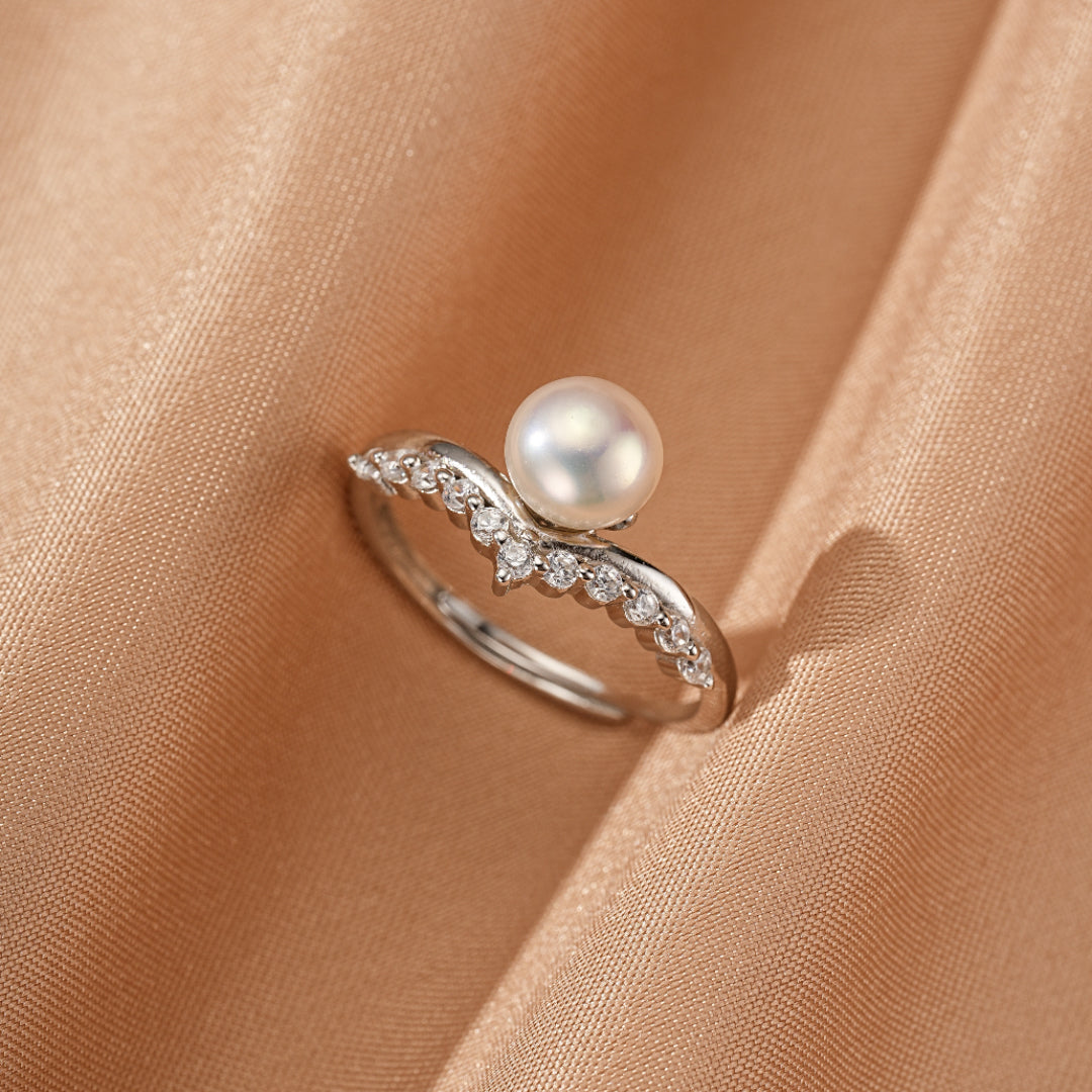 Bague courbe en argent 925 sertie d'une perle blanche et de petits diamants scintillants sur un fond de satin beige satiné satin doré