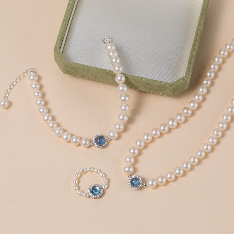 Ensemble de bijoux en argent sterling avec perles et aigue-marine : collier, bracelet et bague, ornés de zirconiums cubiques scintillants autour d'une pierre bleue centrale.