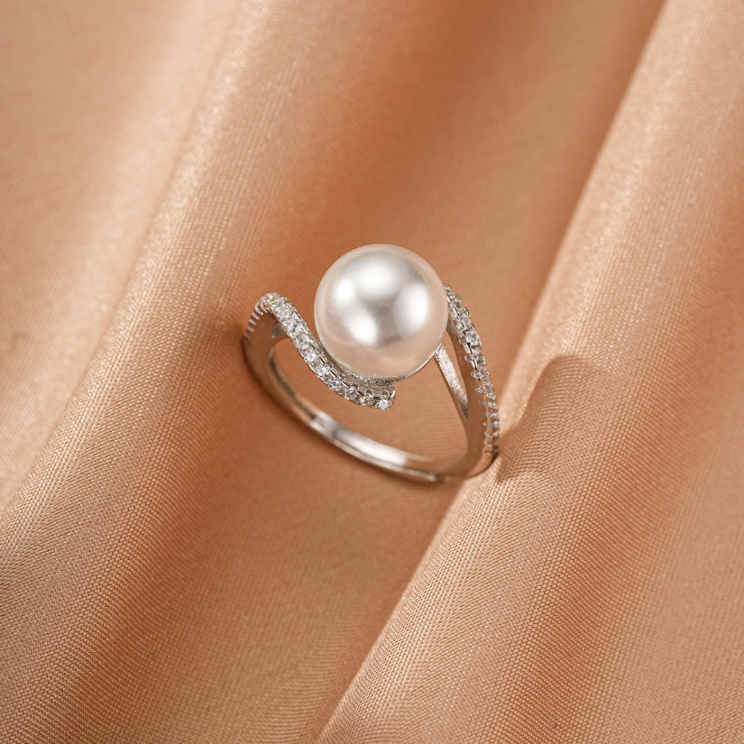 Bague en argent avec une perle blanche centrale et des zircons scintillants sur le corps ondulé de la bague