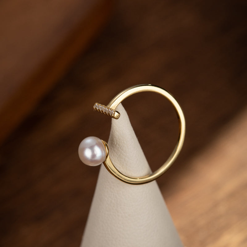 Bague en argent plaqué or avec une perle rose et des diamants incrustés, design moderne et élégant.