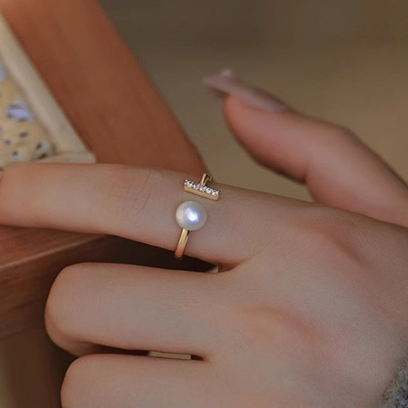 Bague ouverte plaqué or avec une perle blanche centrale et une barre de zirconium sur le dessus.