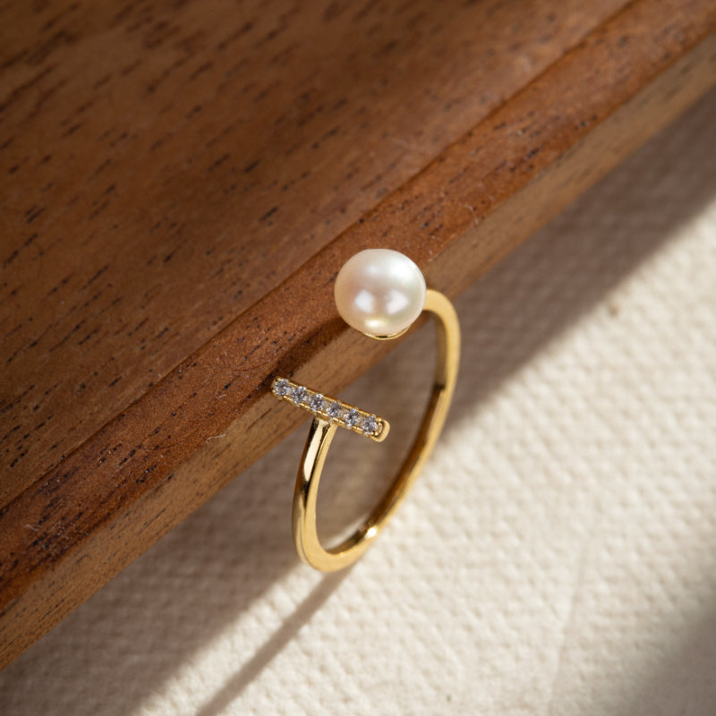 Bague en argent plaqué or sertie d'une perle blanche et de petites pierres scintillantes sur un fond en bois