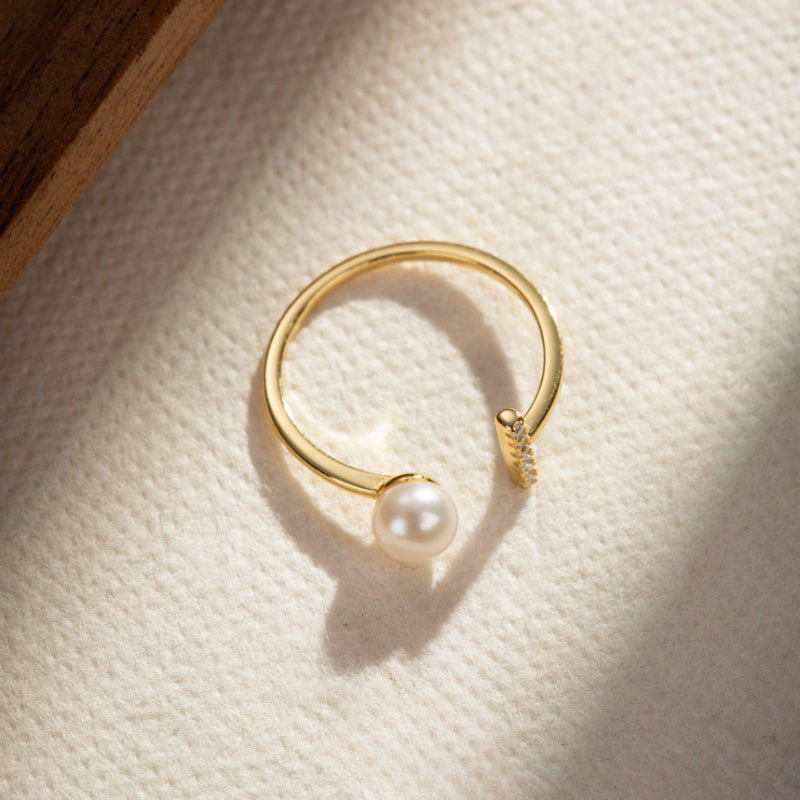 Bague ajustable en argent plaqué or ornée d'une perle et de petites pierres scintillantes.