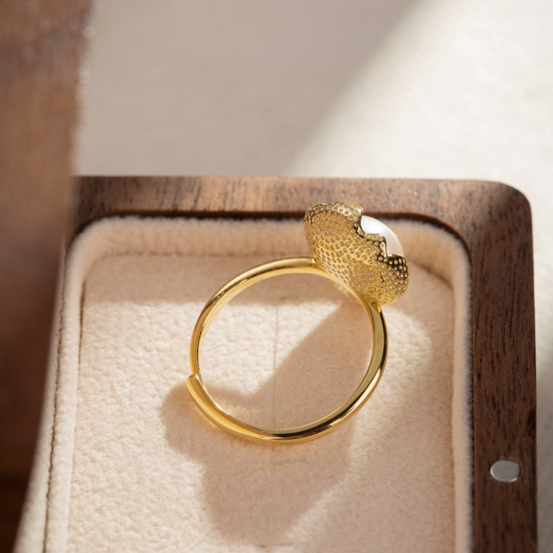 Bague ajustable en argent plaqué or avec une perle blanche et un motif texturé sur le dessus, présentée dans une boîte en bois.