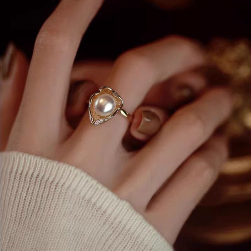 Bague fine en argent plaqué or sertie d'une perle nacrée et de petits cristaux, style vintage, mise en valeur sur un doigt portant un pull blanc.