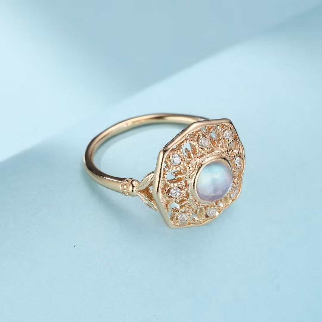 Bague antique en argent plaqué or avec une pierre de lune bleu opalescente et des petites pierres d'accent sur un fond bleu clair.