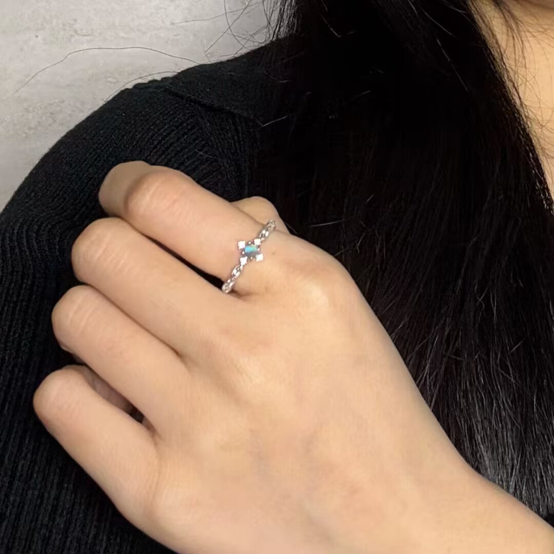 Bague fine en argent avec une petite pierre bleue rectangulaire au centre, portée sur l'annulaire d'une main.