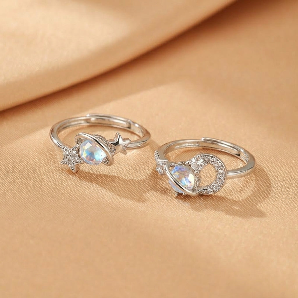 Deux bagues en argent ornées de pierres de lune bleutées et d'étoiles, l'une en forme de planète et l'autre avec un design de constellation.