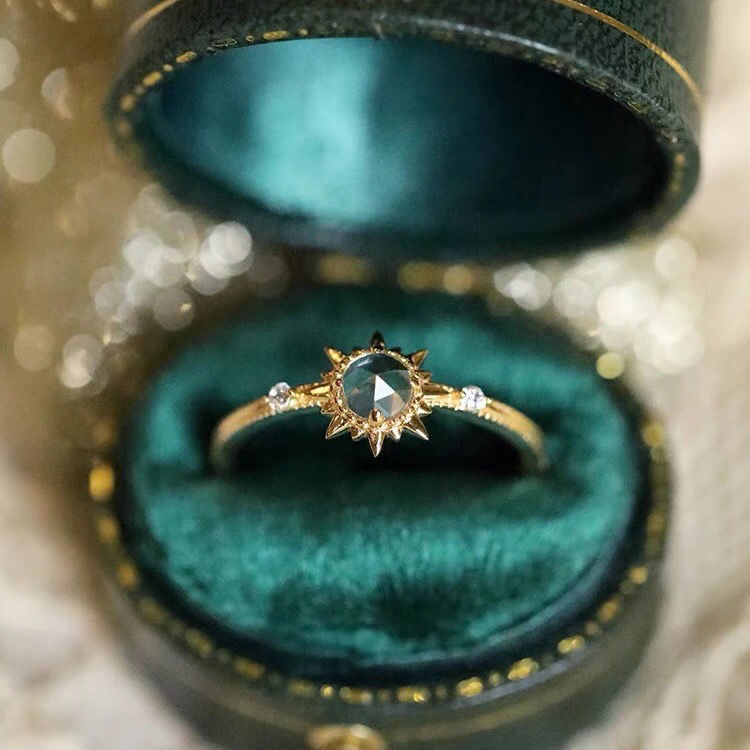 Bague en argent plaqué or avec un quartz clair central taillé en losange, entouré de pointes rayonnantes et de deux petits diamants sur chaque côté, présentée dans une boîte bijou verte.