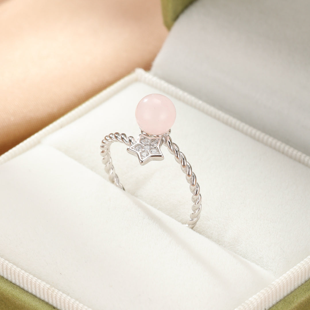 Bague en argent fin avec une perle de quartz rose et une étoile ornée de zirconium, sur un fond blanc.