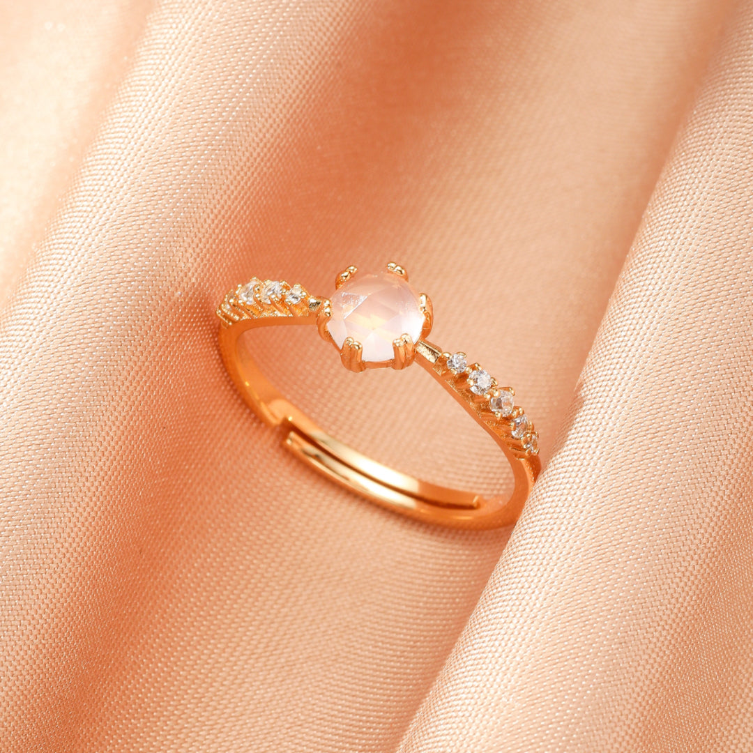 Bague réglable en argent plaqué or 10 carats avec un quartz rose rond et des zircons cubiques incrustés sur le côté, sur un fond satiné rose pâle.