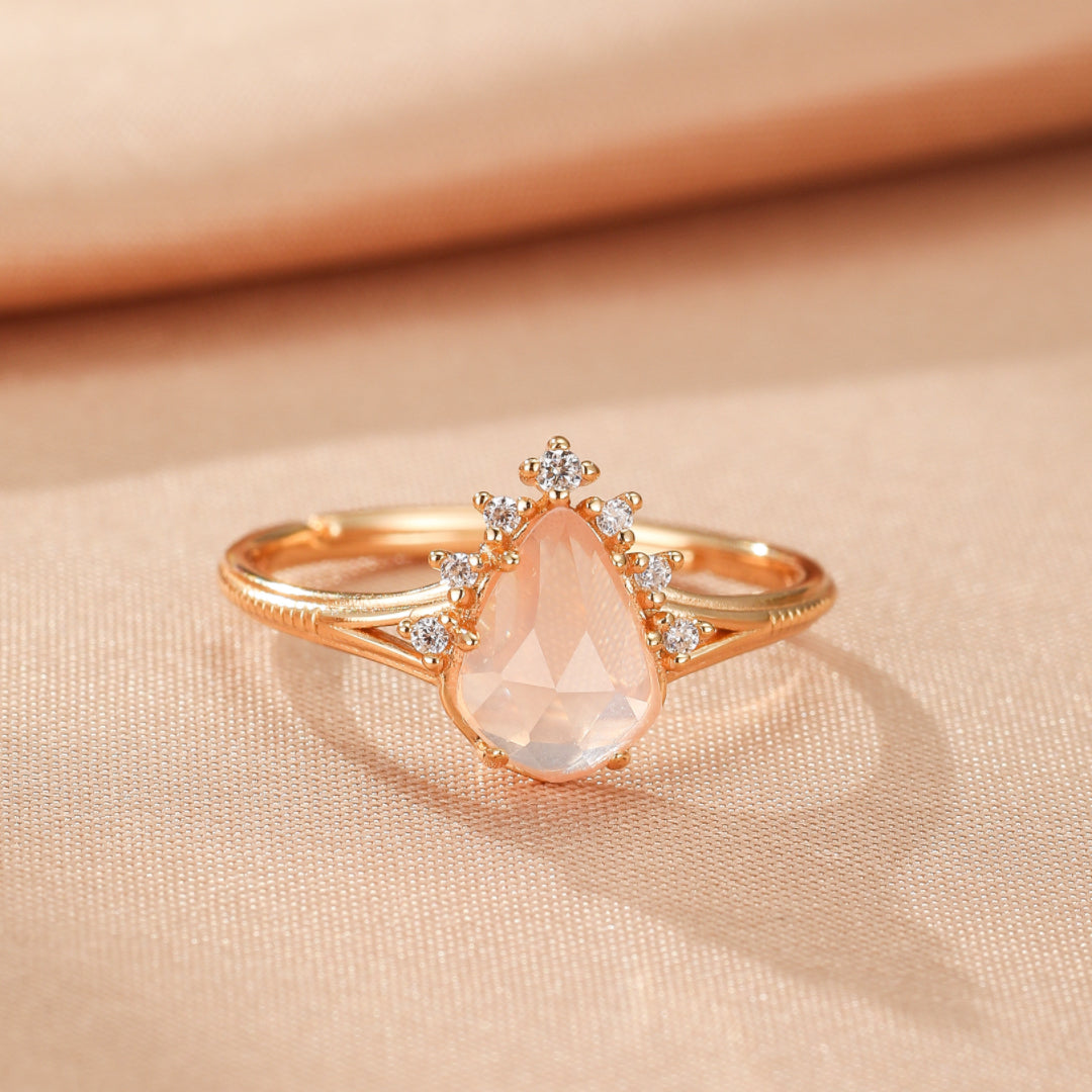 Bague en argent plaqué or 9K avec une pierre de quartz rose en forme de goutte, sertie sur un anneau fin orné de petites pierres scintillantes.