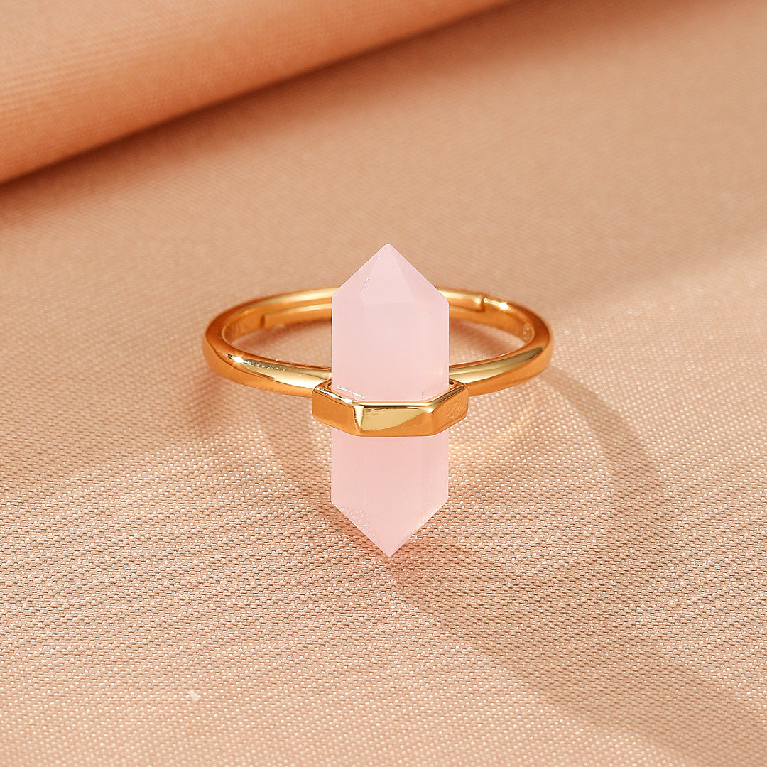 Bague tendance en plaqué or 10K avec un cristal de quartz rose facetté en forme de pointe hexagonale au centre, sur un fond textile doux couleur pêche.
