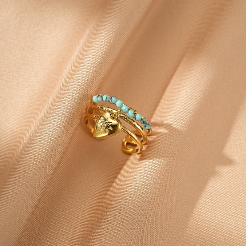 Bague dorée à plusieurs anneaux superposés, ornée d'une breloque cœur sertie d'une petite pierre et d'une chaîne de petites perles turquoise.